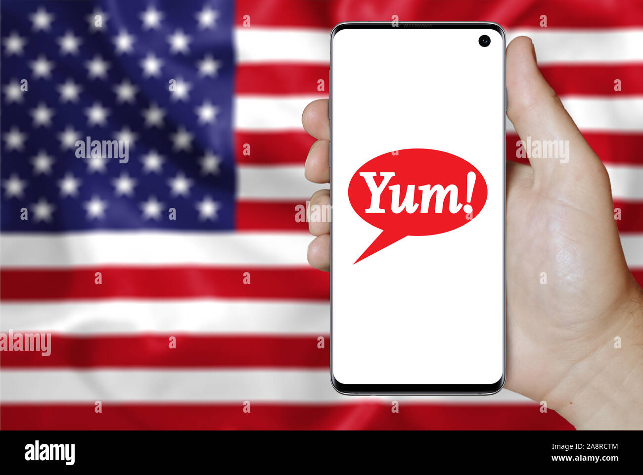 Logo of public company Yum! Brands Inc displayed on a smartphone. Flag of USA background. Credit: PIXDUCE Stock Photo