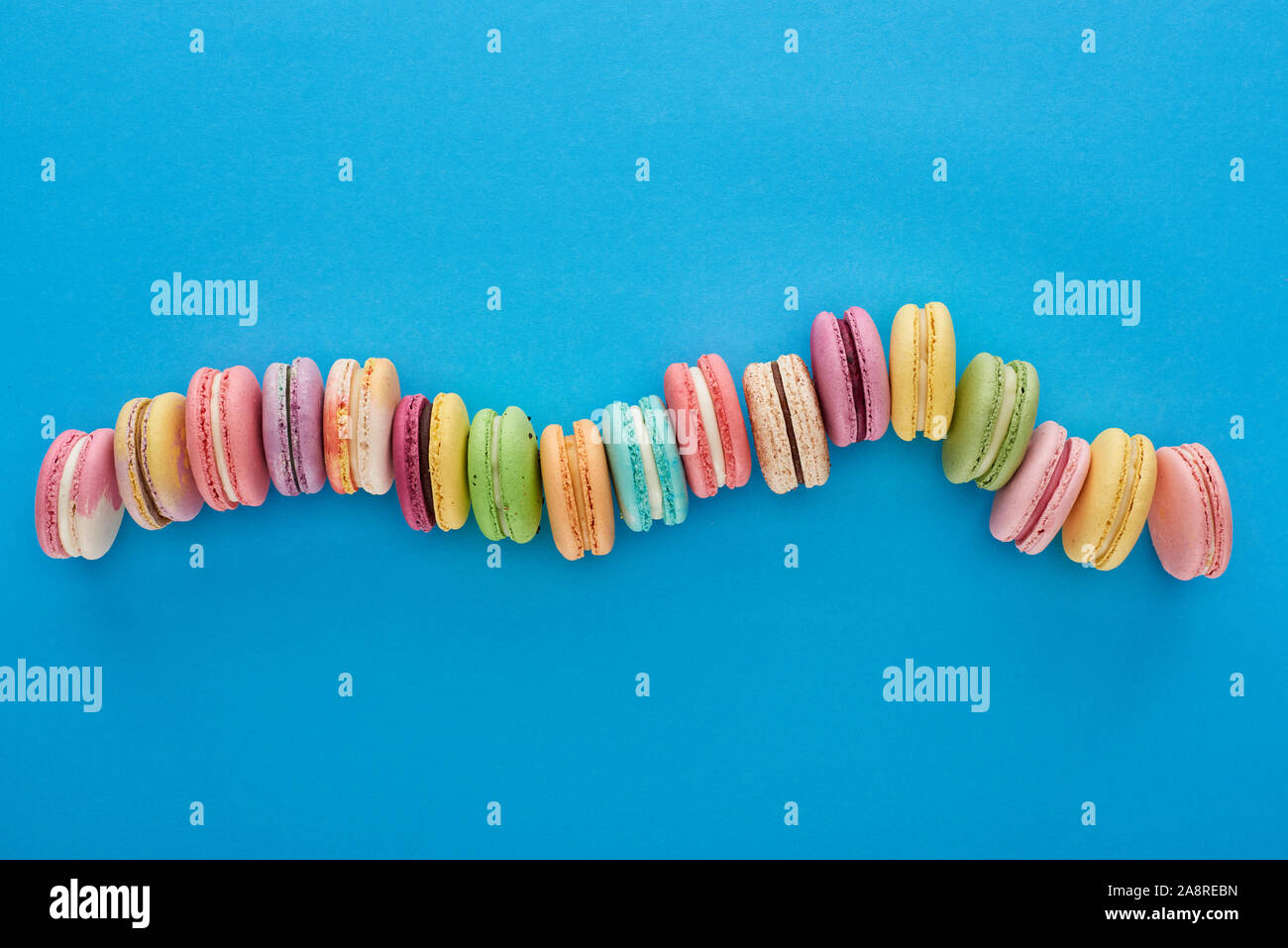 top view of multicolored delicious French macaroons in curved line on blue bright background Stock Photo