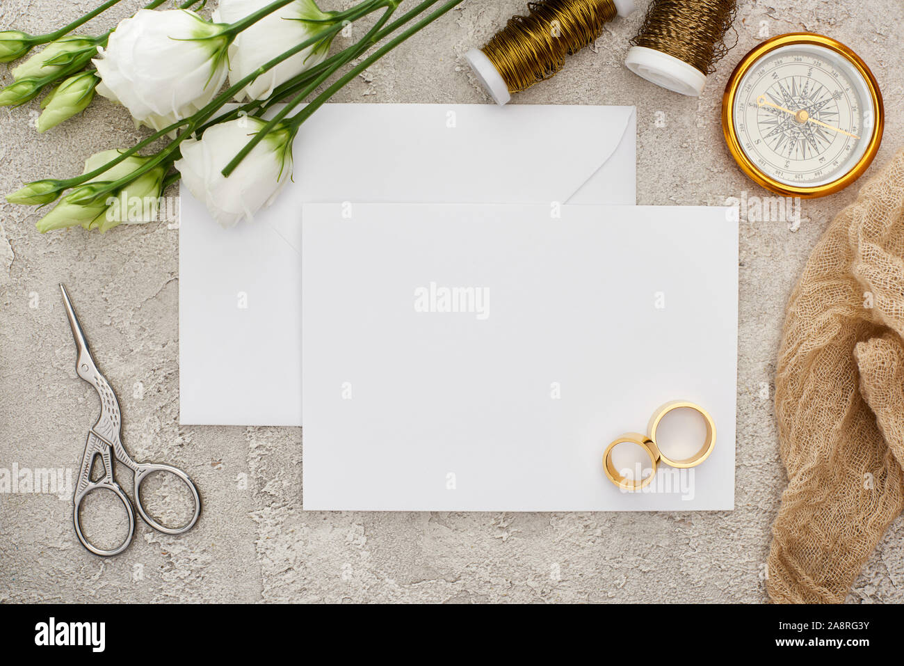 top view of wedding rings on empty card near white eustoma flowers, spools, scissors and golden compass on grey surface Stock Photo