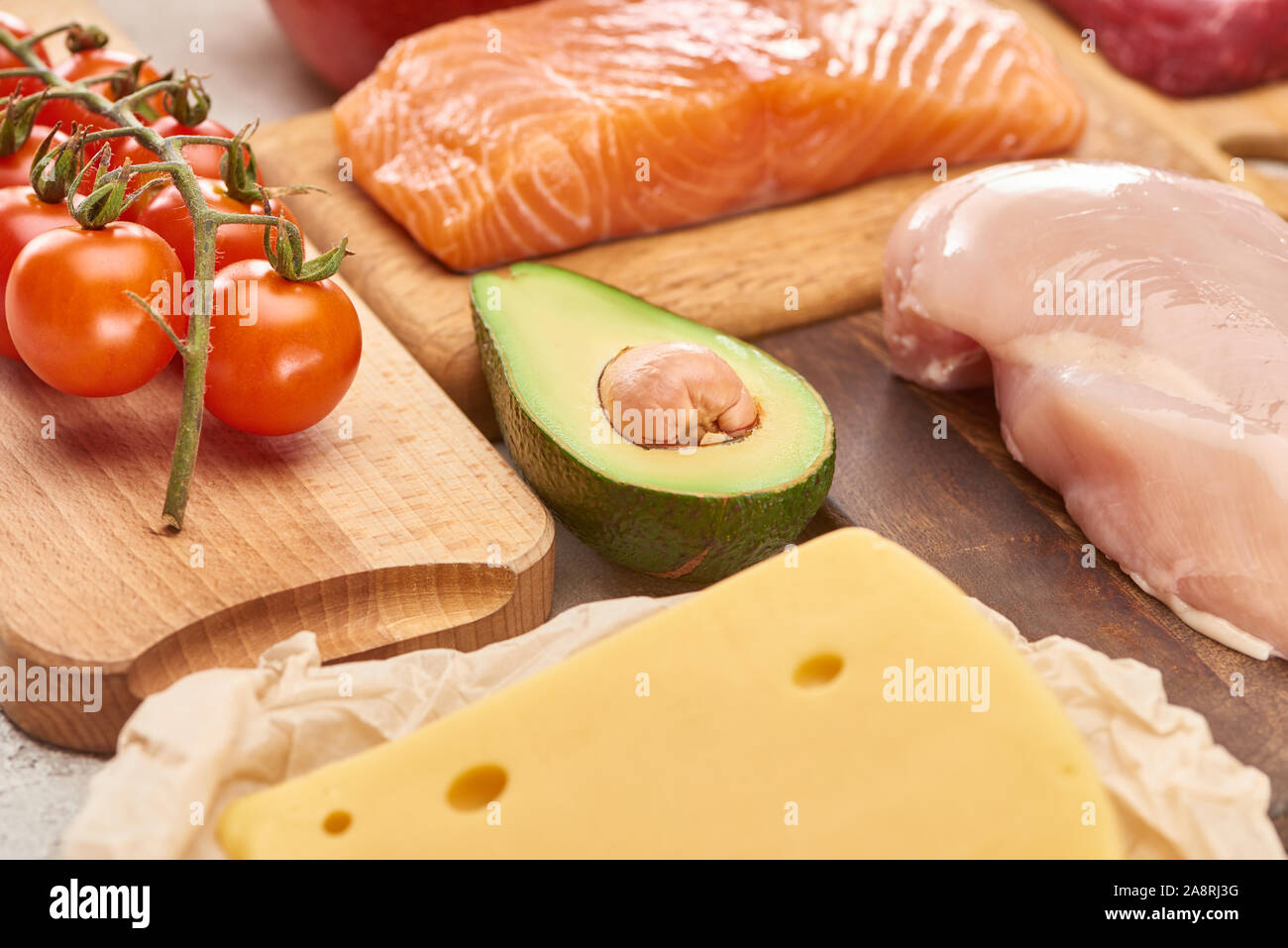 Fresh raw fish, poultry, cheese, branch of cherry tomatoes and half of avocado on wooden cutting boards Stock Photo