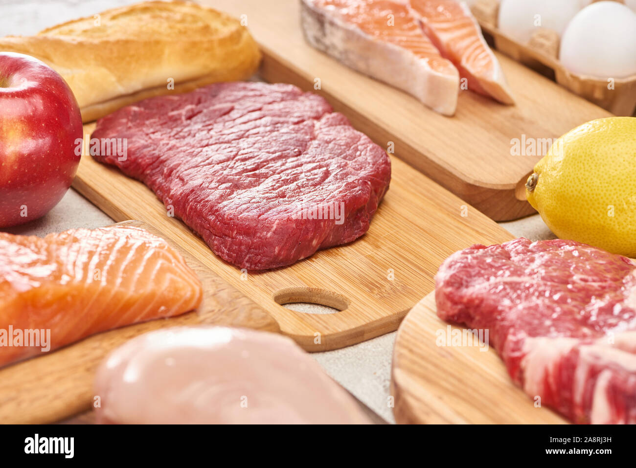 Fresh raw meat, fish, poultry on wooden cutting boards near apple, lemon, baguette and eggs Stock Photo