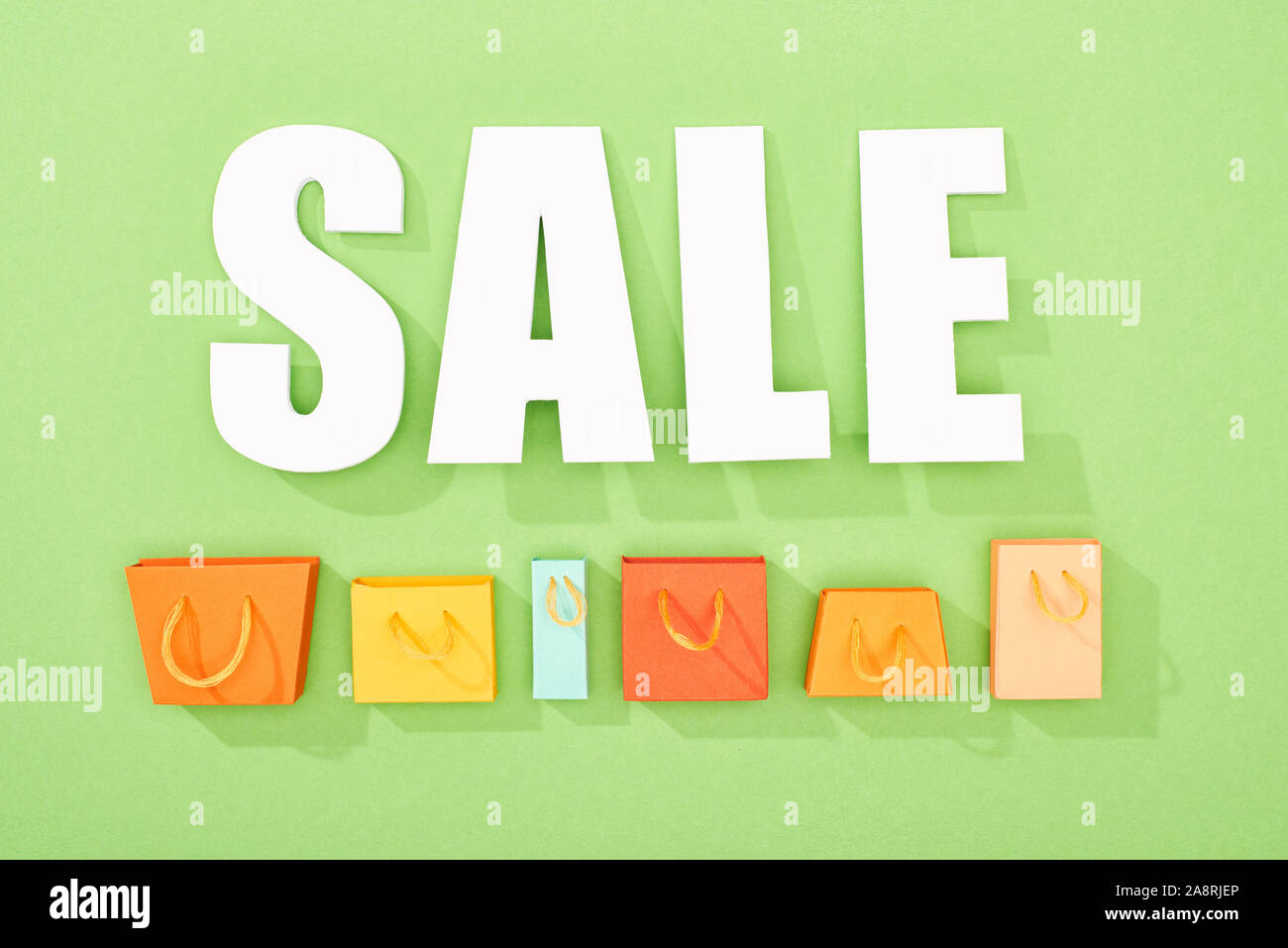 top view of decorative shopping bags and white sale lettering on green background Stock Photo