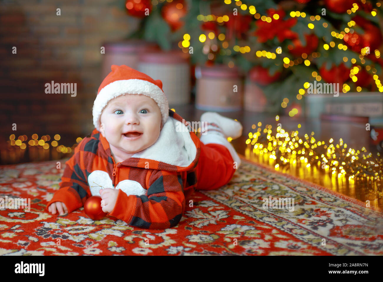 Little six month old baby dressed as Santa Claus. Background for christmas card. child looks down at place for inscription on background of luminous g Stock Photo