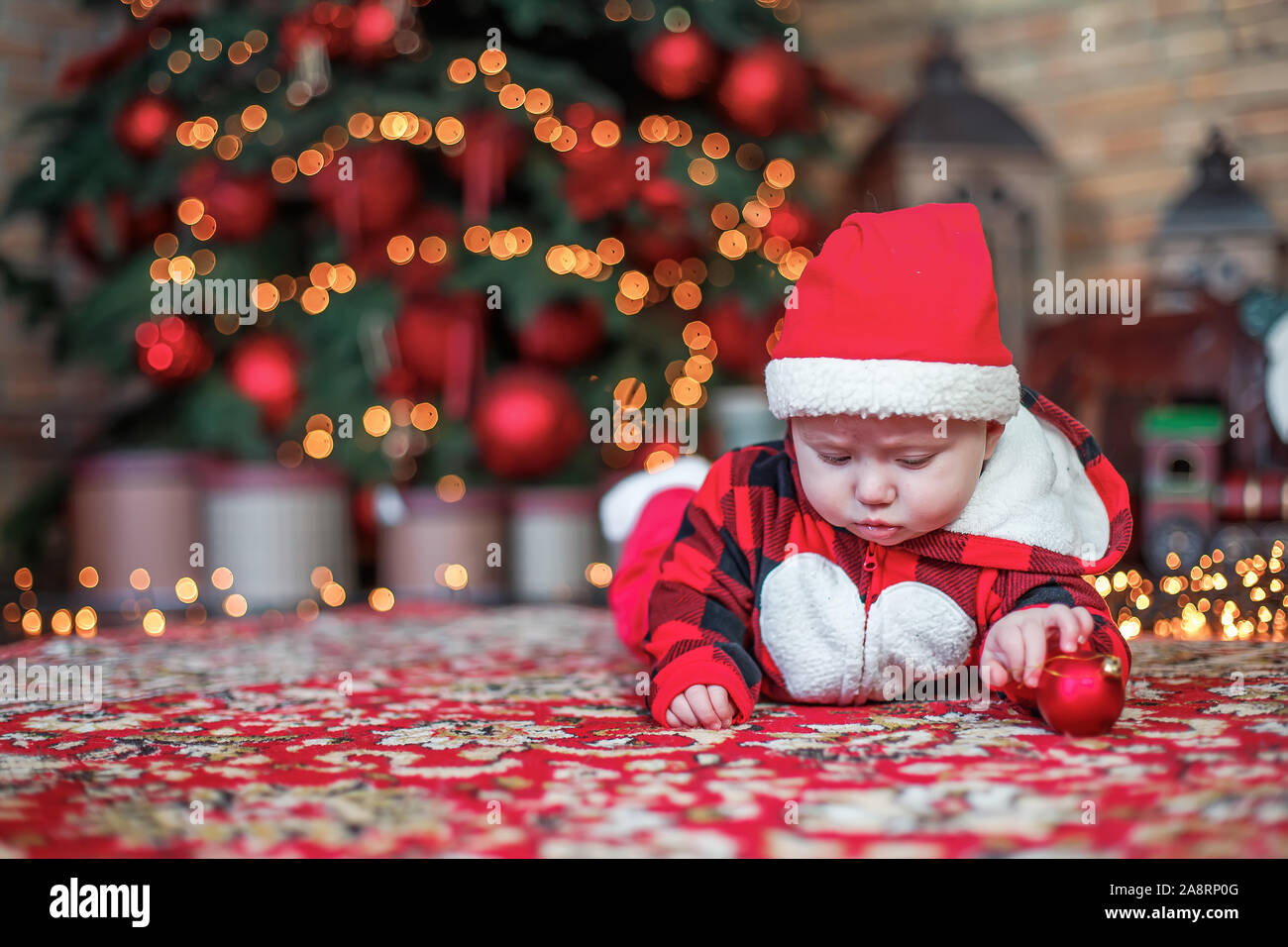 Little six month old baby dressed as Santa Claus. Background for christmas card. child looks down at place for inscription on background of luminous g Stock Photo