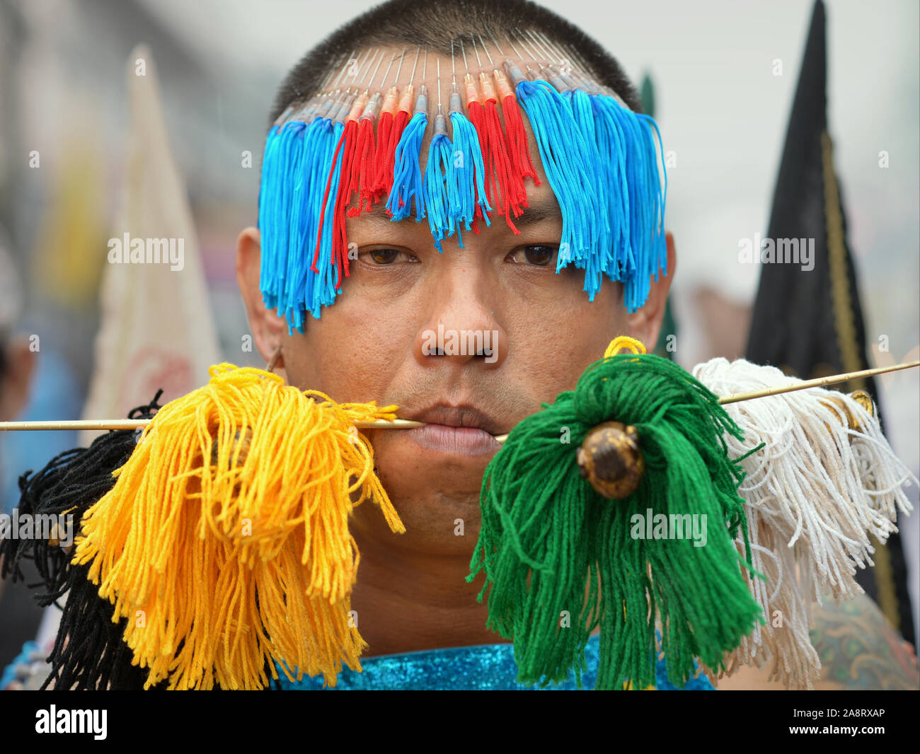 Thai Chinese Taoist devotee (mah song) pierces his tongue and earlobes with long pins/skewers and his forehead with decorated hypodermic needles. Stock Photo