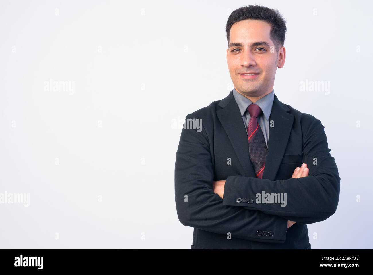 Portrait of happy Persian businessman in suit smiling with arms crossed ...