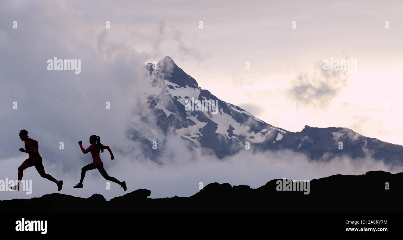 Running fit athletes people trail running with mountain summit background. Man and woman silhouetteon run training outdoors active fit lifestyle. Stock Photo