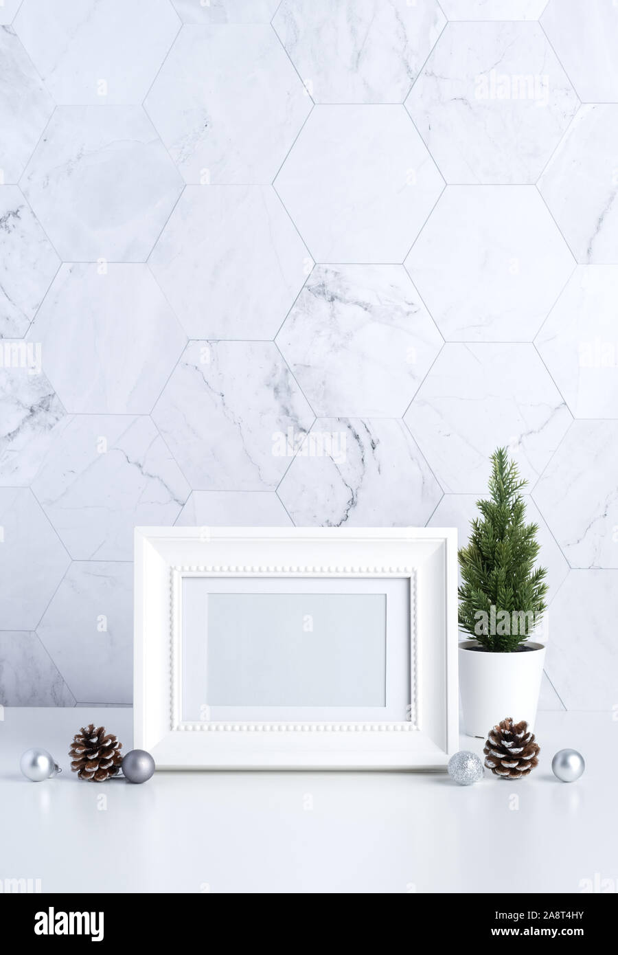 white vintage photo frame with christmas tree,pine cone and decor xmas ball on white table and marble tile wall background.clean minimal simple style. Stock Photo