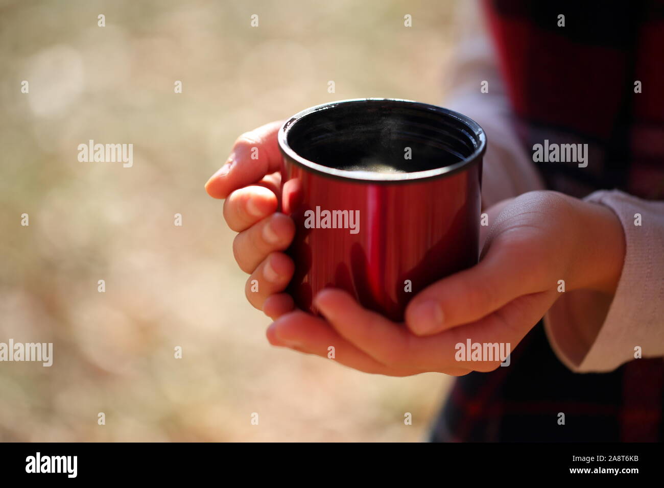 Children's hands hold a red mug with tea in the autumn park Stock Photo