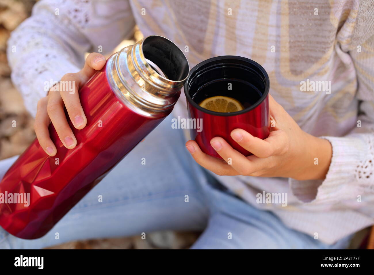 Children's hands hold a red mug with tea in the autumn park Stock Photo
