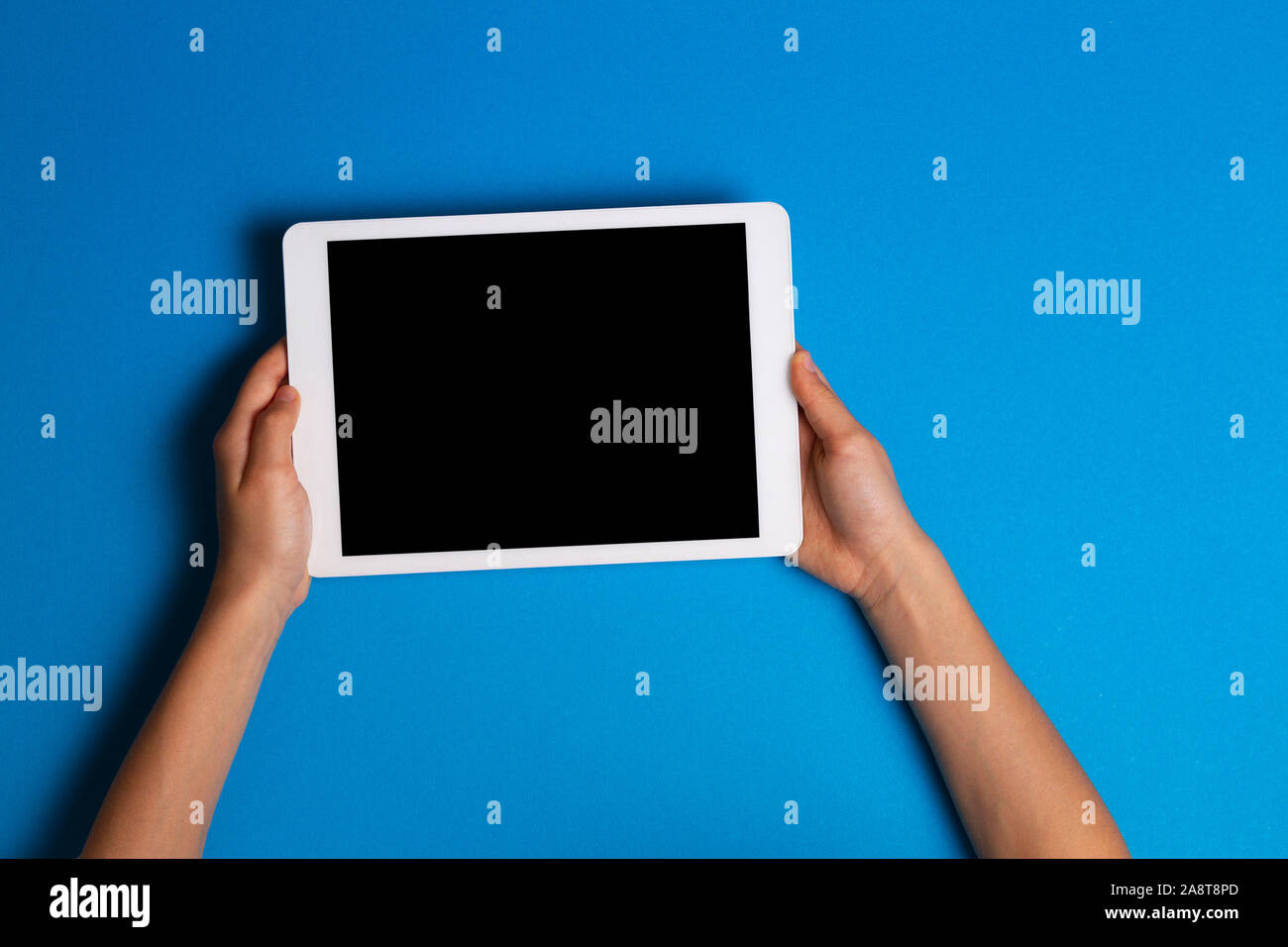 Kid hands holding white tablet computer on light blue background Stock Photo