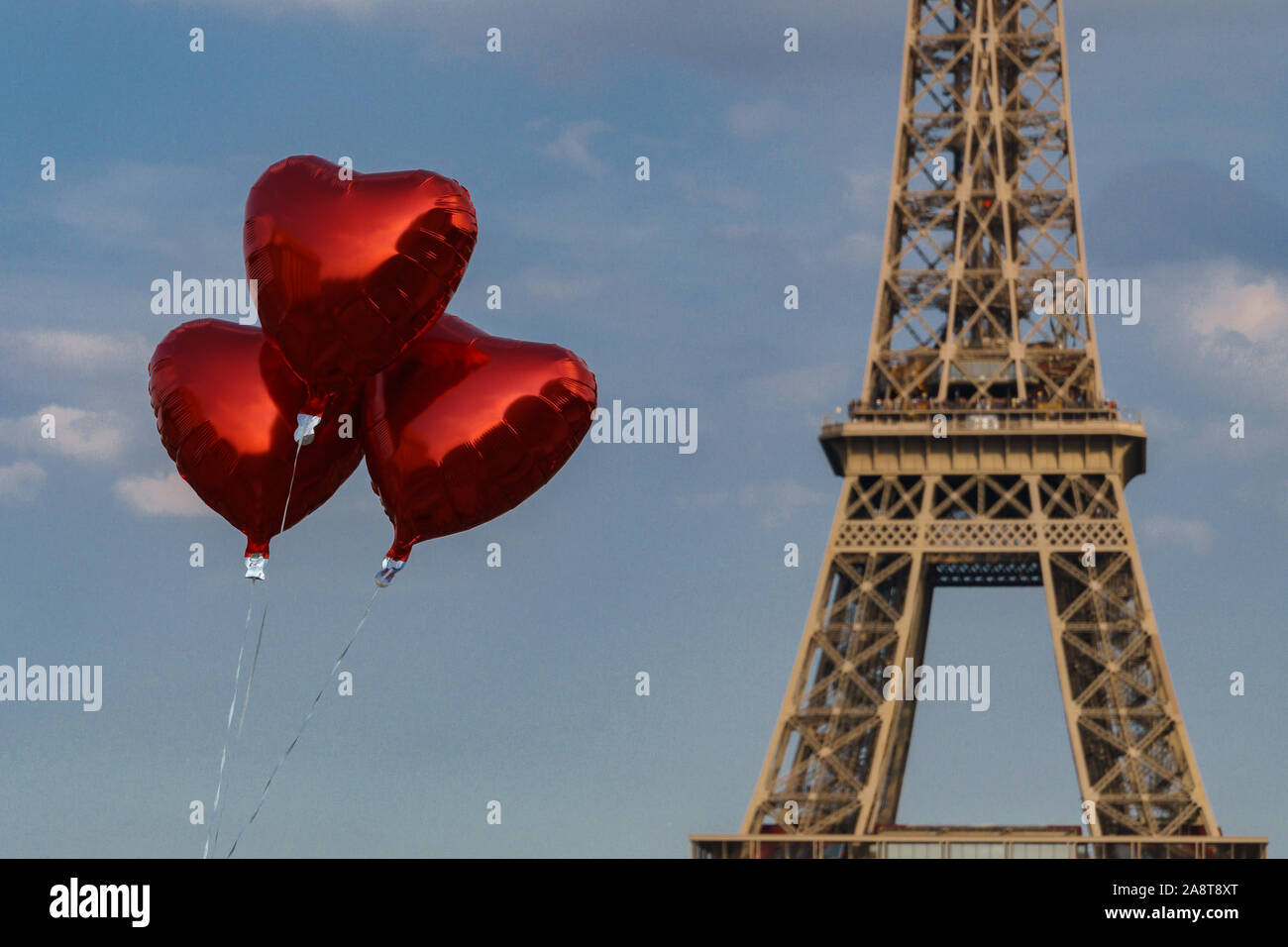 Heart shaped metallic red balloons in front of the eiffel tower with blue sky and some fluffy clouds Stock Photo