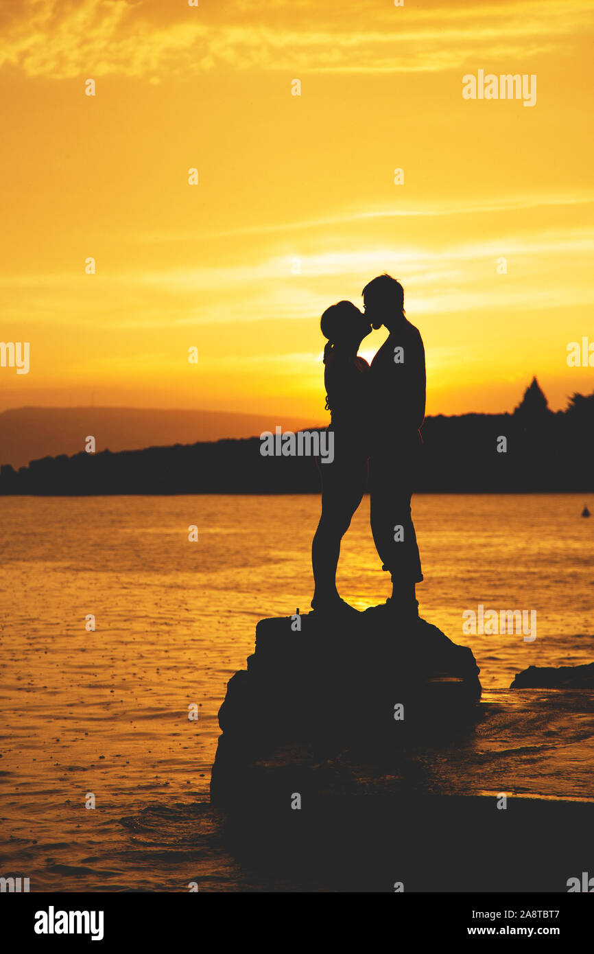 Silhouettes of a couple in love kiss at sunset by the sea Stock Photo ...