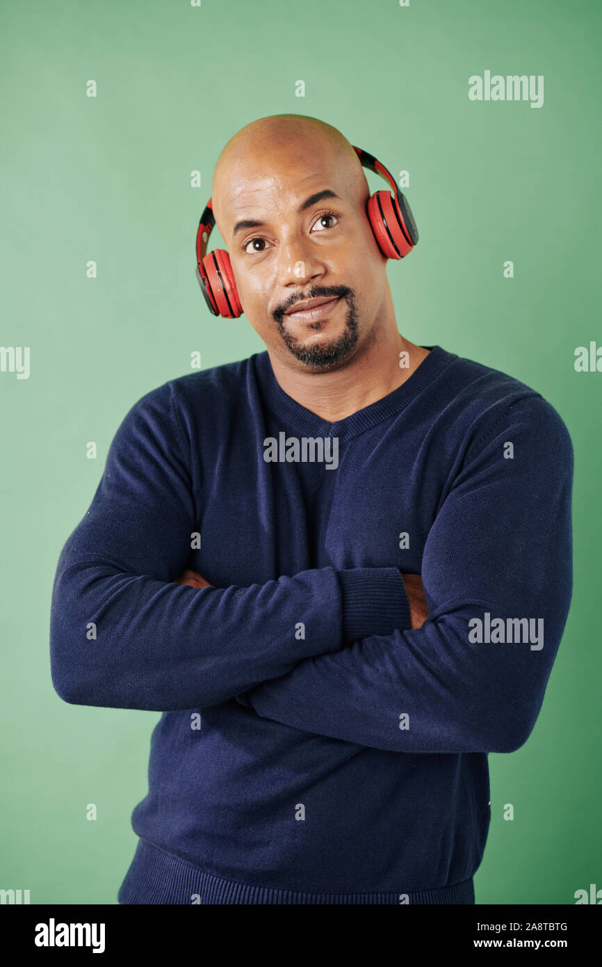 Portrait of strong man in tight sweater folding arms and enjoying listening to music in headphones Stock Photo