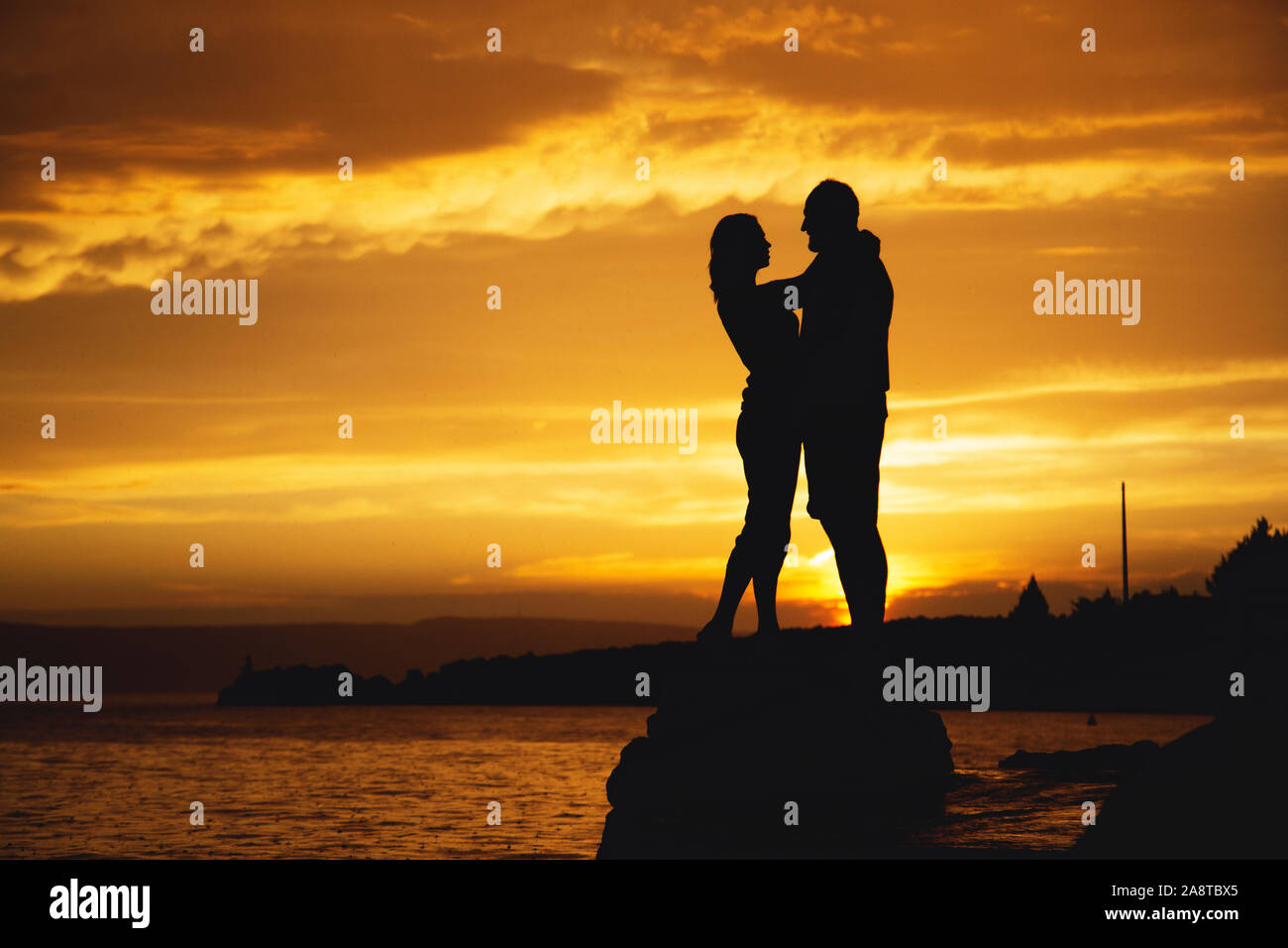 Silhouettes of a couple in love kiss at sunset by the sea Stock Photo ...