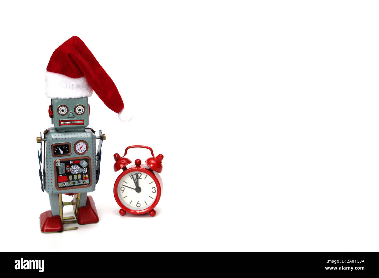 Retro robot with Santa hat is ready to meet Christmas and New Year. Next to the robot are a red clock, which is almost midnight. The concept is time, Stock Photo