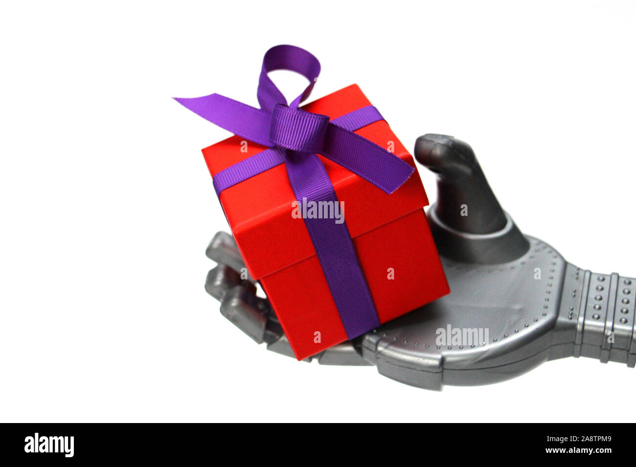 Robot hand holds a red gift box. The gift is tied with a beautiful purple bow. Smart robot gives gifts. New Year. Birthday. White background. Concept Stock Photo