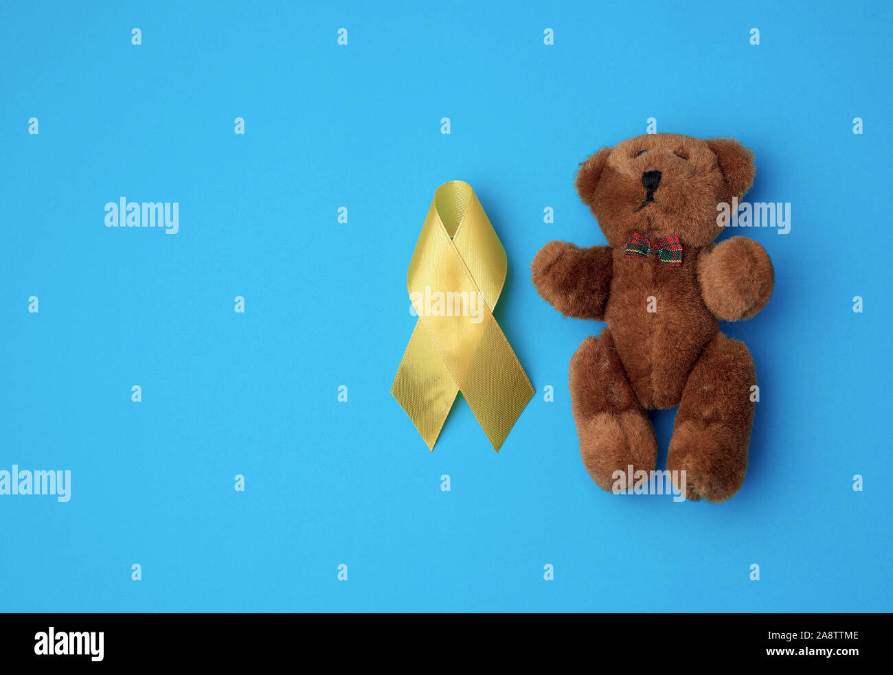 brown teddy bear and yellow silk ribbon on a blue background, concept of the fight against childhood cancer. problem of suicides and their prevention, Stock Photo