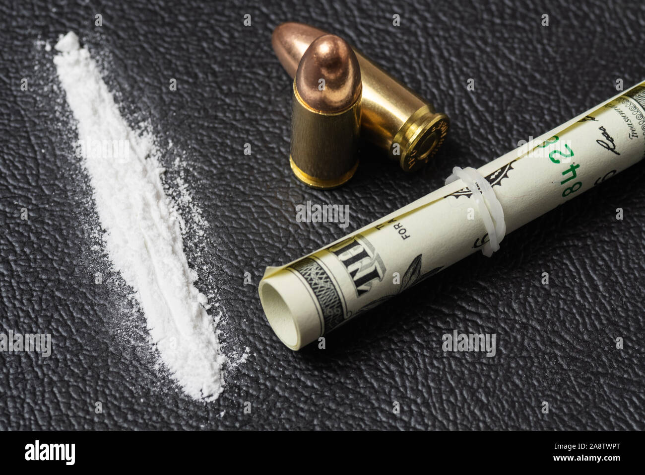 Dollar bill scroll, cocaine powder and two 9 mm bullets on black surface. Conceptual mockup of illegal drug dealing, trafficking, war on drugs. Stock Photo