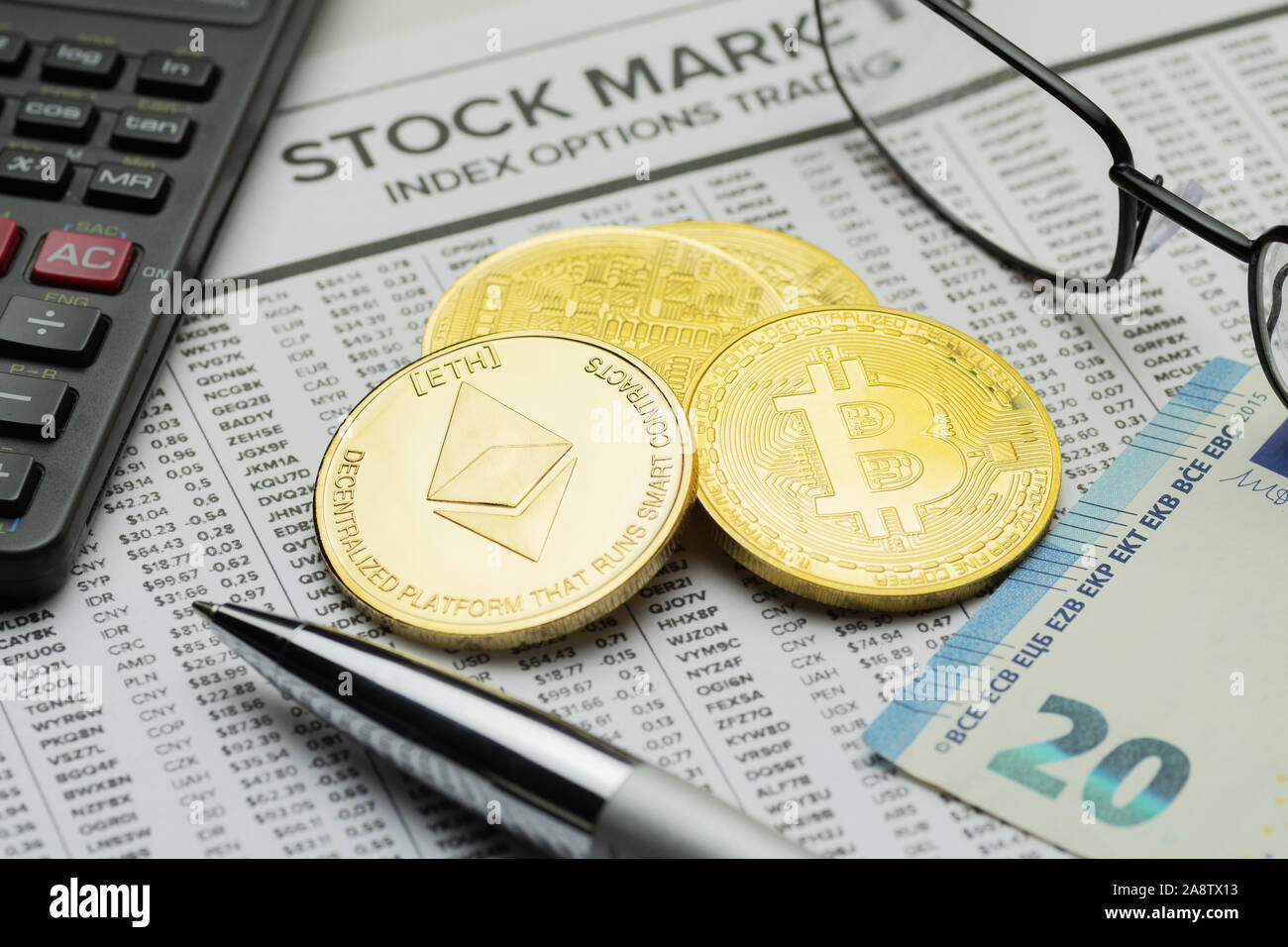 Closeup of golden Bitcoin and Ethereum coins on mockup newspaper financial page with visible eyeglasses, calculator, ballpoint pen and Euro banknote Stock Photo