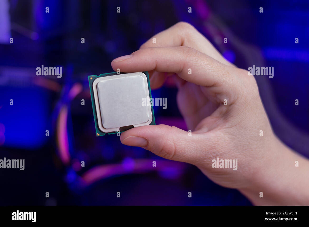 Hand holds a modern processor. Computer with RGB illumination in background. Close-up. Stock Photo
