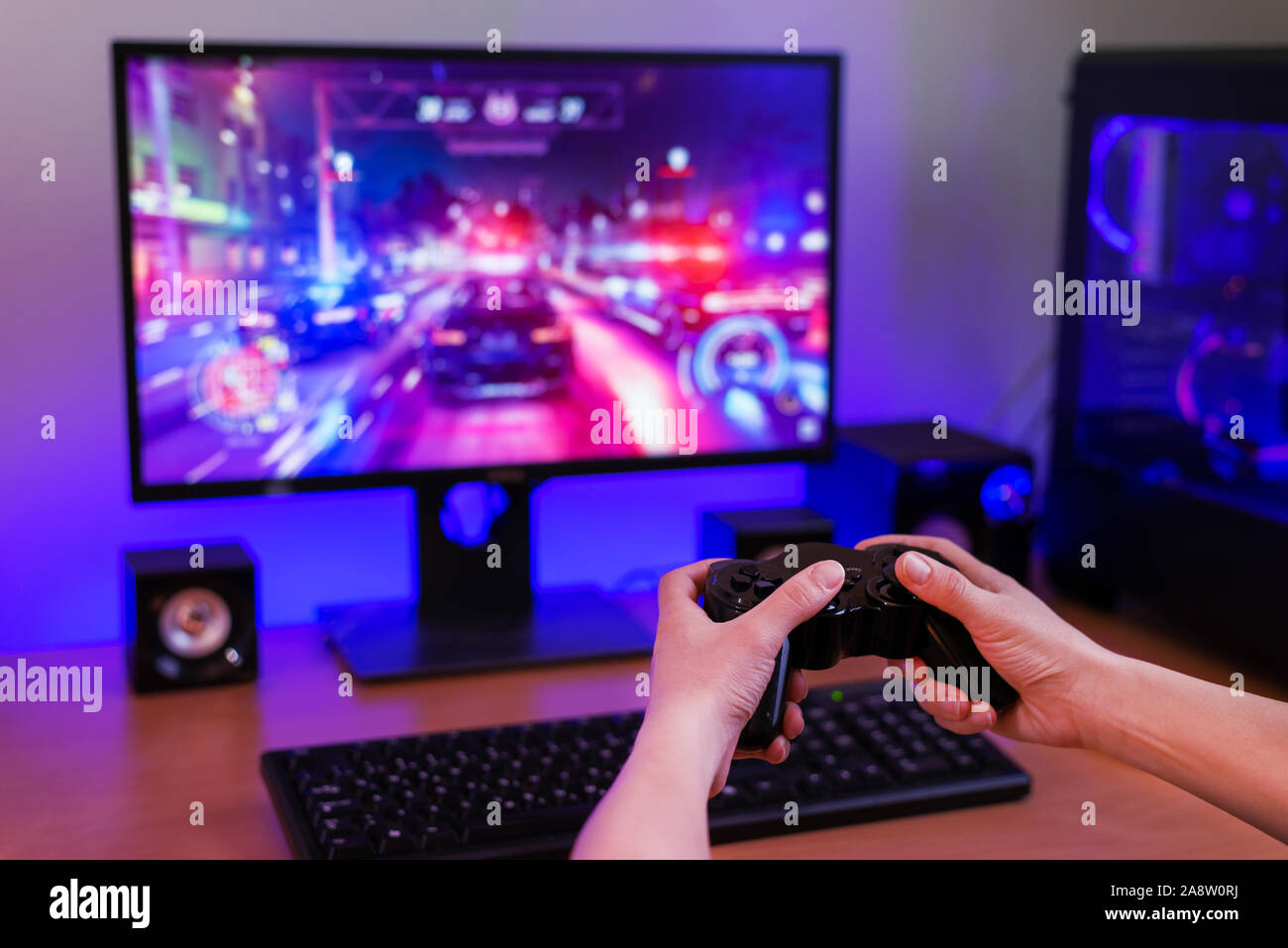 Playing racing games on computer concept. Hand holds the joystick. In the background is a gaming computer with RGB light. Stock Photo
