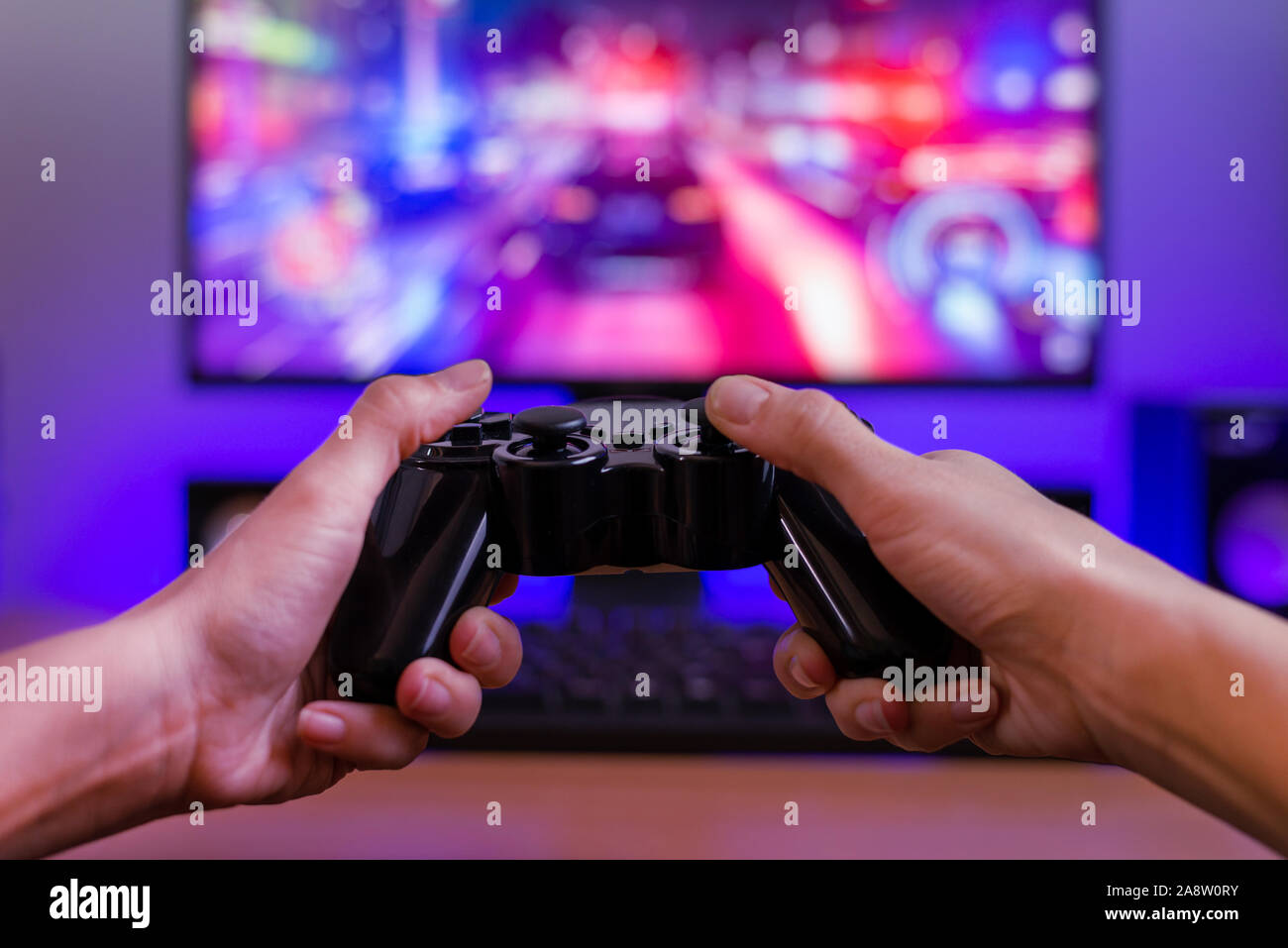 Joypad in hands. Gaming concept. Computer display with racing game and rgb light in background. Stock Photo