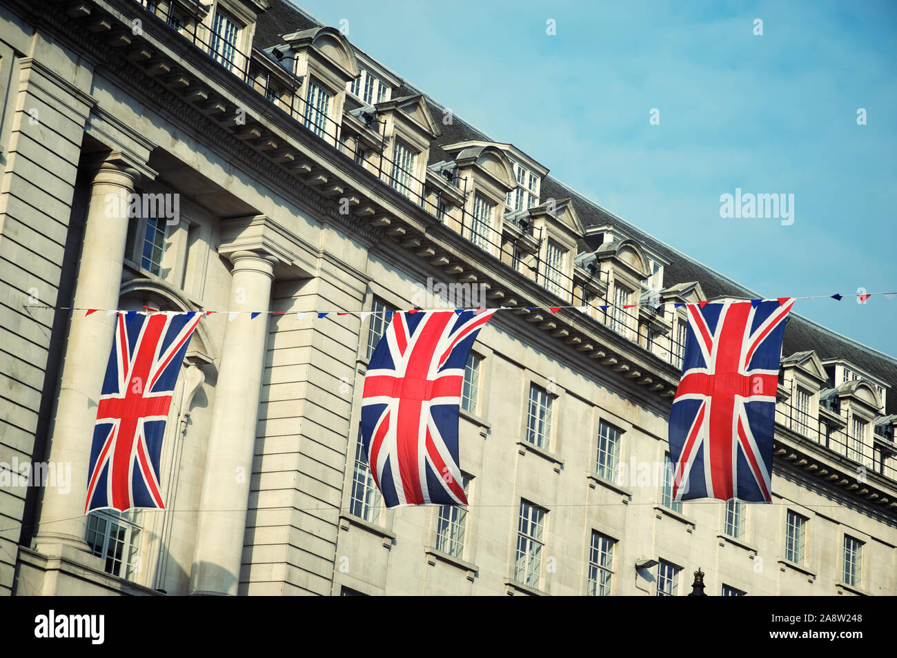 Union Jack flag decorations strung above the streets of London, UK under soft blue sky Stock Photo