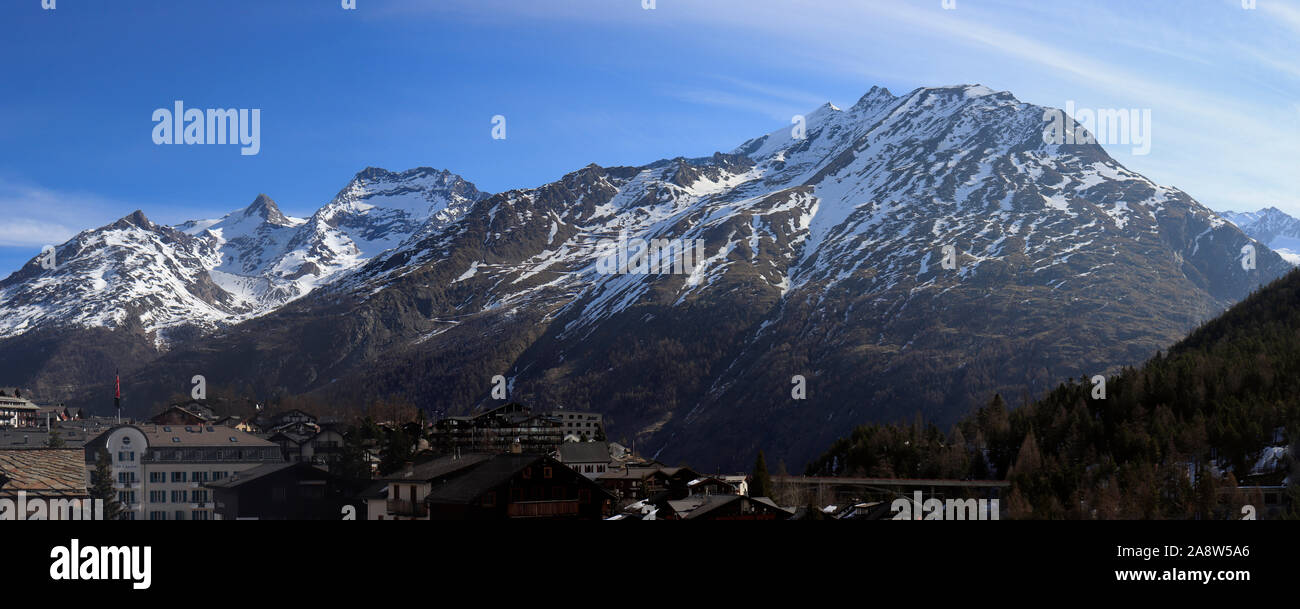 Saas Fee, Switzerland - march 2019: Traditional wooden Hotels and Huts in Saas-Fee Ski Resort with morning light on mountain range. Stock Photo