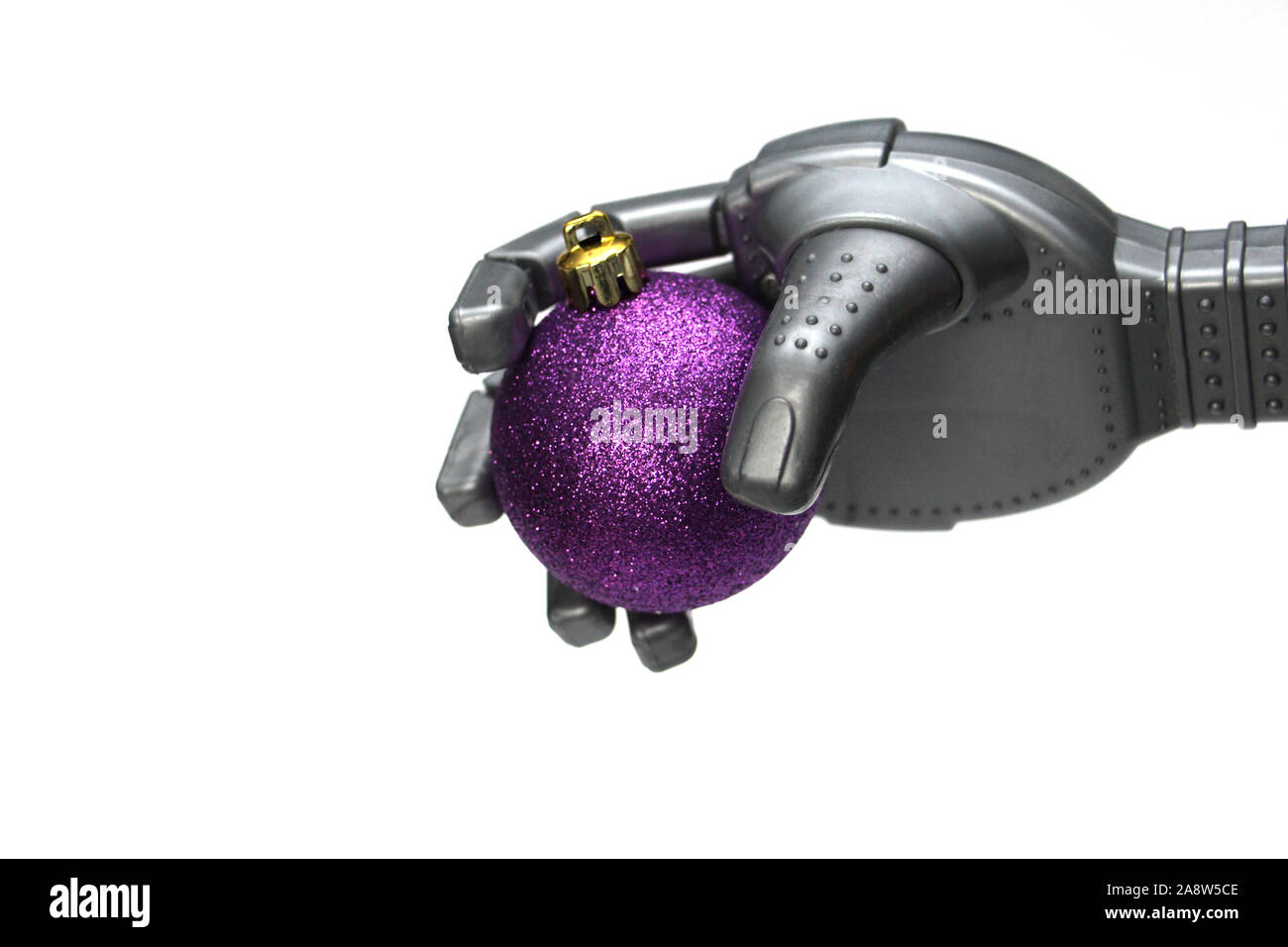 A robot holds a purple Christmas tree decoration in his hand. Purple christmas ball in the robot hand. Christmas and New Year celebration concept in r Stock Photo