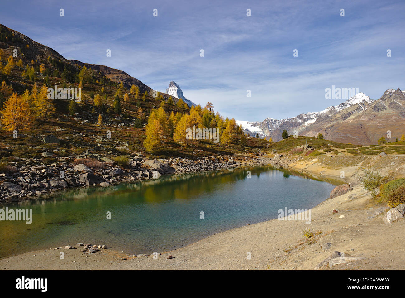 Little lake gruensee with yellow and orange colored Larch forest in autumn in Zermatt. Matterhorn peeking over hill. Stock Photo