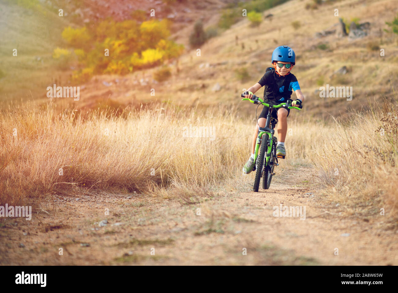 Happy kid boy of 7 years having fun in autumn park with a bicycle on beautiful fall day. Active child wearing bike helmet Stock Photo