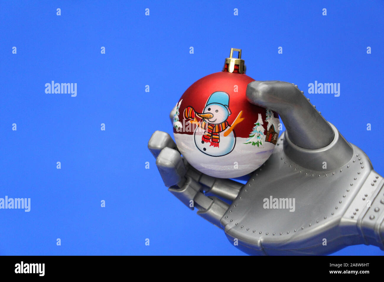 A robot holds a Christmas tree decoration in his hand. Christmas ball with a snowman in the hand of a robot. Concept of celebrating Christmas and New Stock Photo