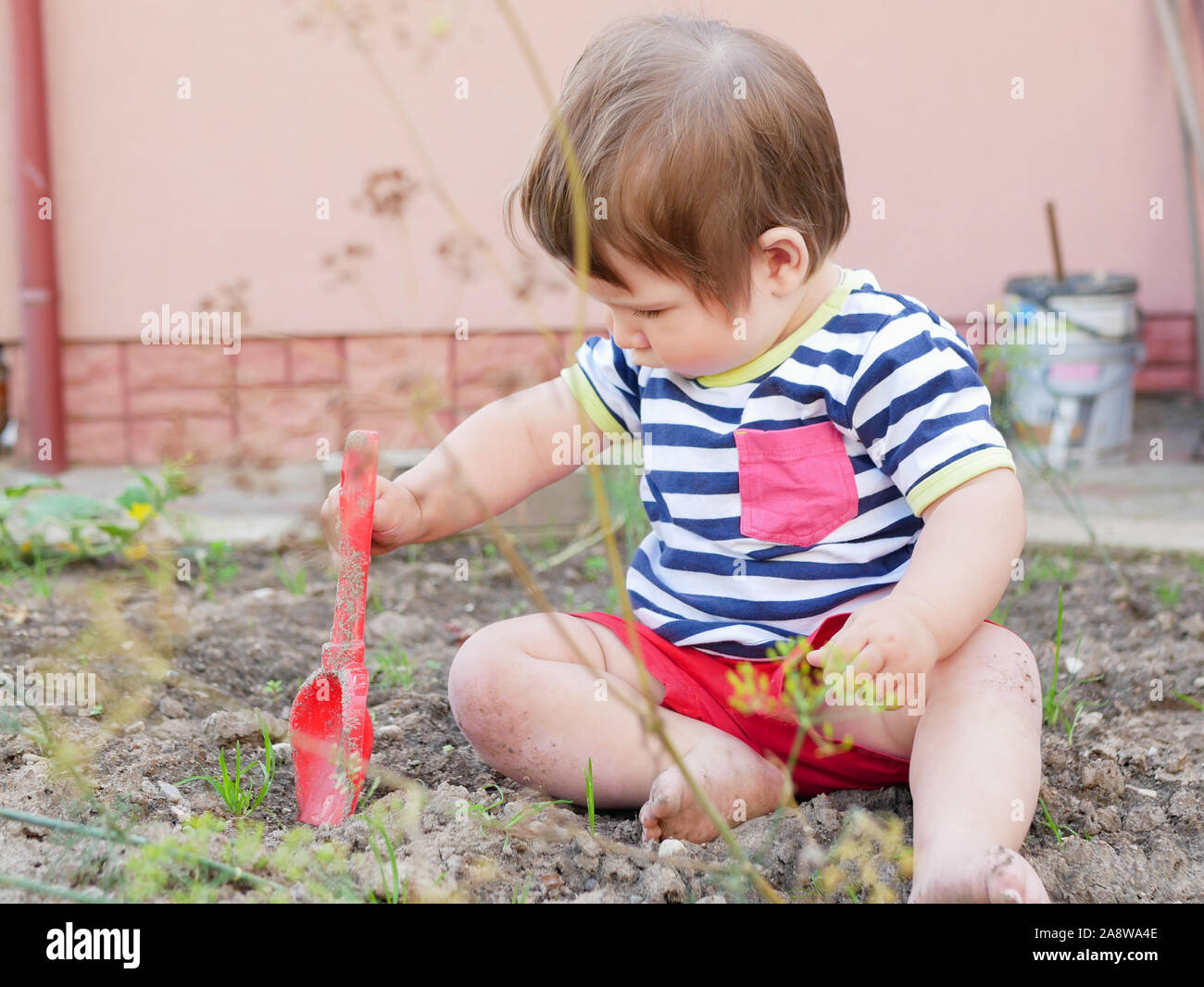 A boy plays with a spatula on the street. Baby boy and red shovel. Boy 0-1 years old Stock Photo