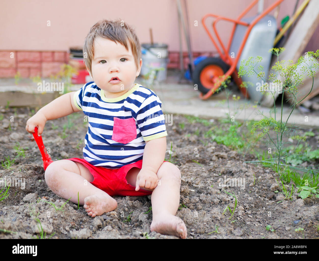 A boy plays with a spatula on the street. Baby boy and red shovel. Boy 0-1 years old Stock Photo