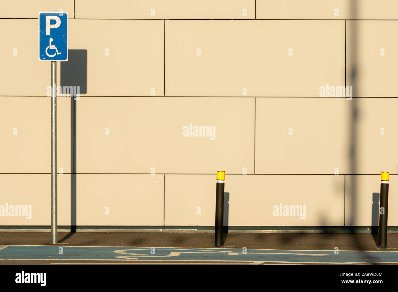 Empty disabled handicap parking space bay with blue marking and handicapped sign symbol casting shadows on a wall. Stock Photo