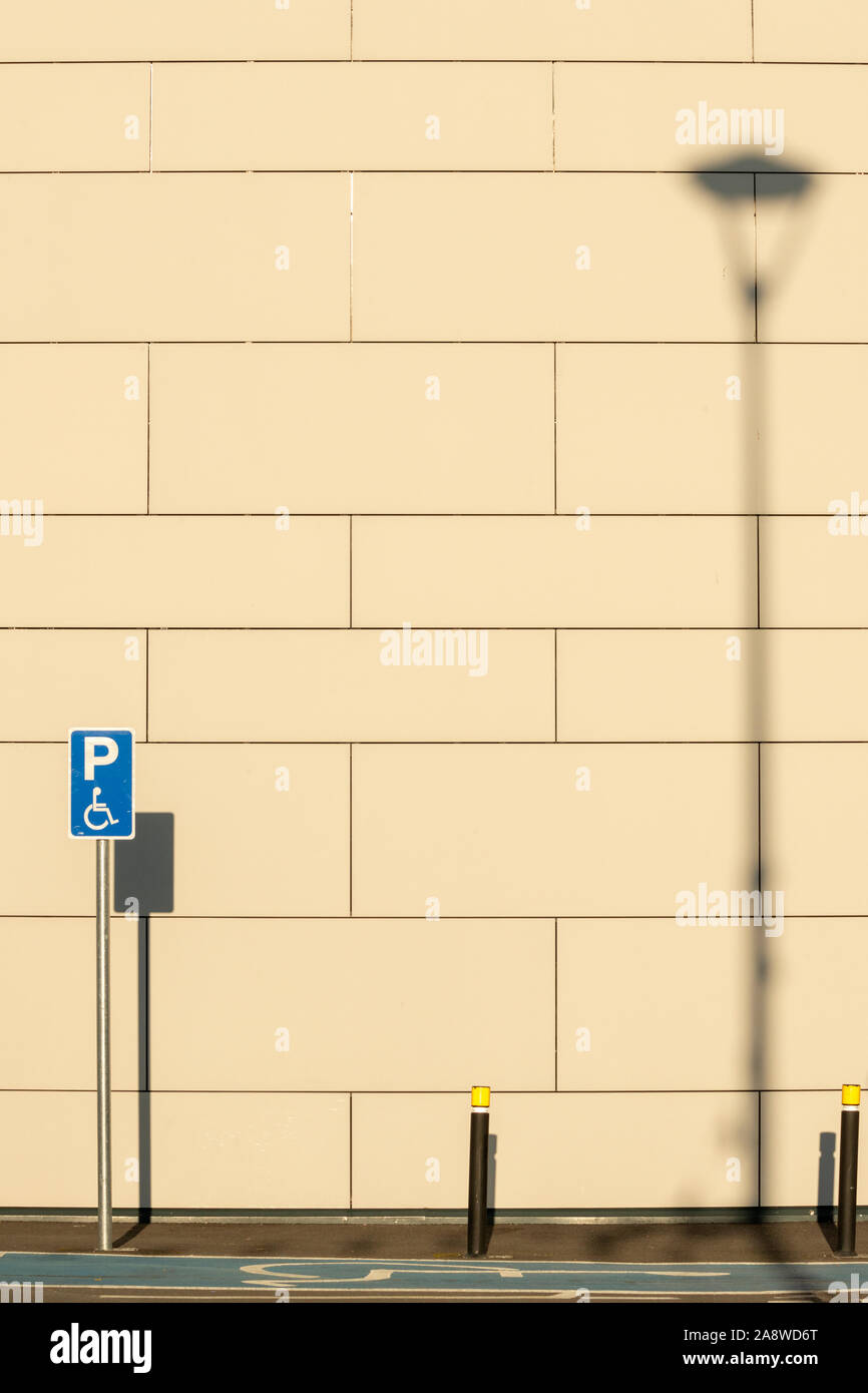 Empty disabled handicap parking space bay with blue marking and handicapped sign symbol casting shadows on a wall. Stock Photo