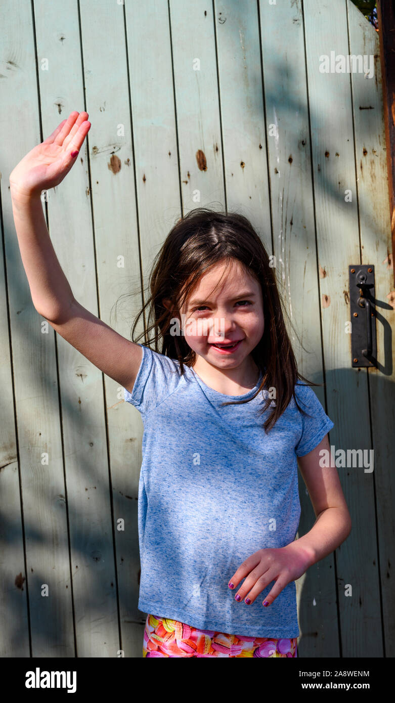 Young girl waving from her back garden gate Stock Photo