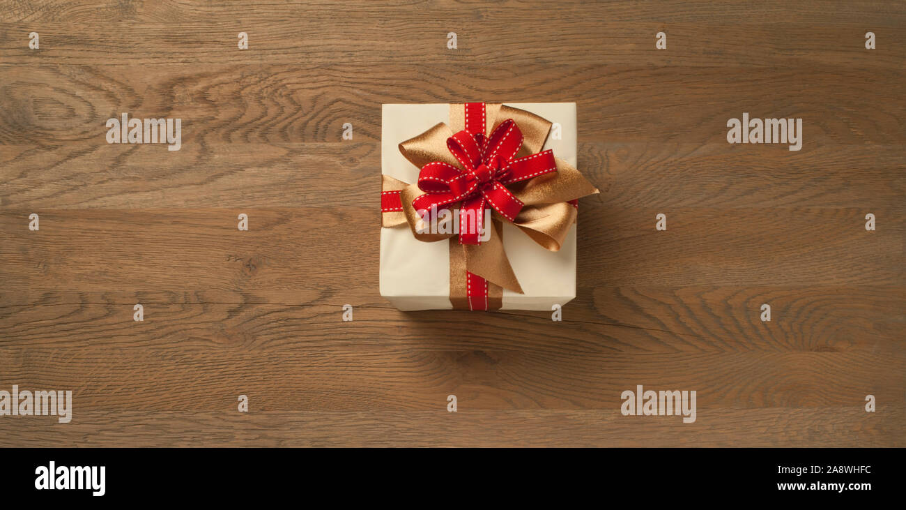 christmas gift box tied with red and golden bow over a wooden table ...