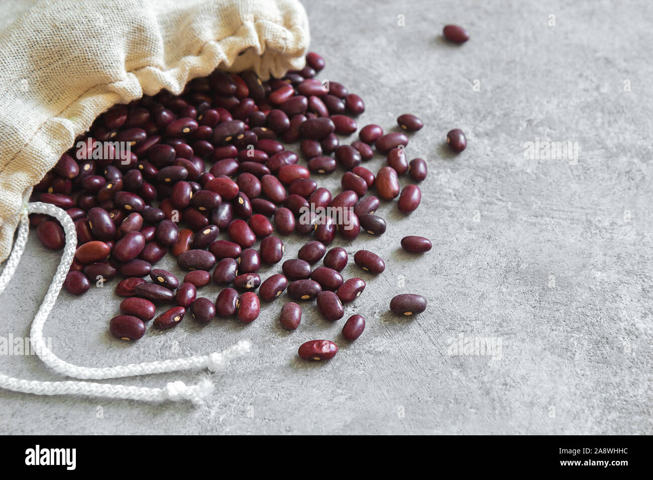 Red beans in a reusable eco bag are scattered on a gray concrete background. Horizontal photo with place for text. Stock Photo