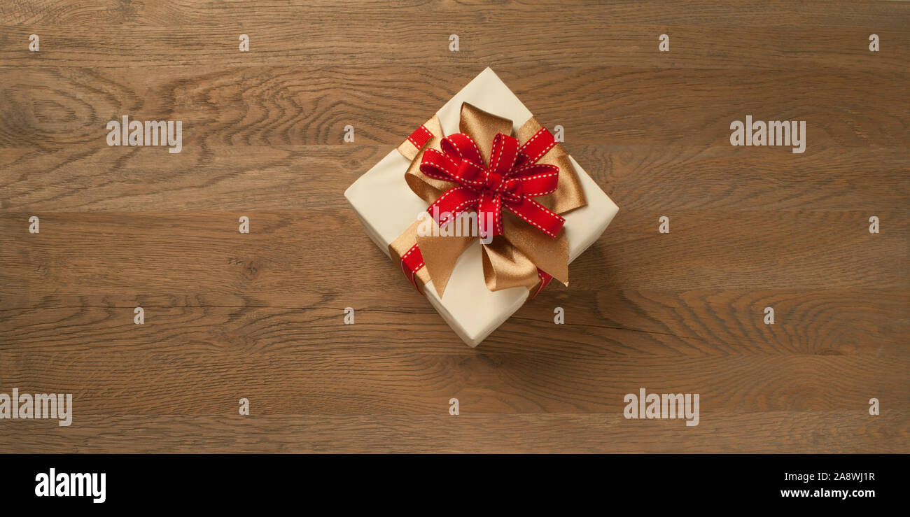 christmas gift box tied with red and golden bow over a wooden table ...