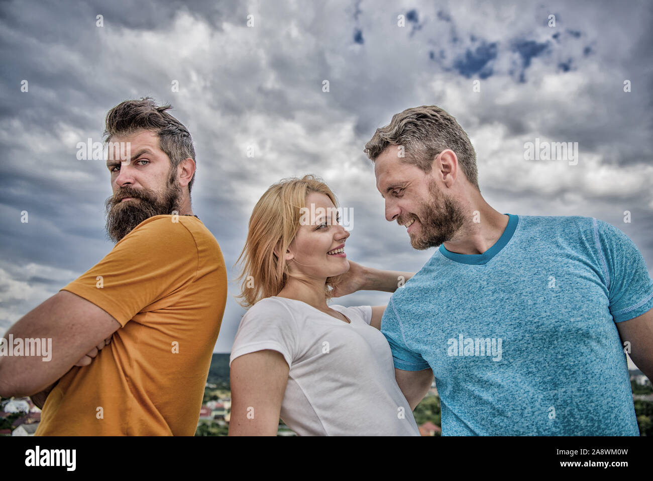 Offended partner still suffers. Couple and rejected partner. How get over breakup for guys. Ruined relationships. Psychology of breakup. Girl stand between two men. What do when you feel rejected. Stock Photo