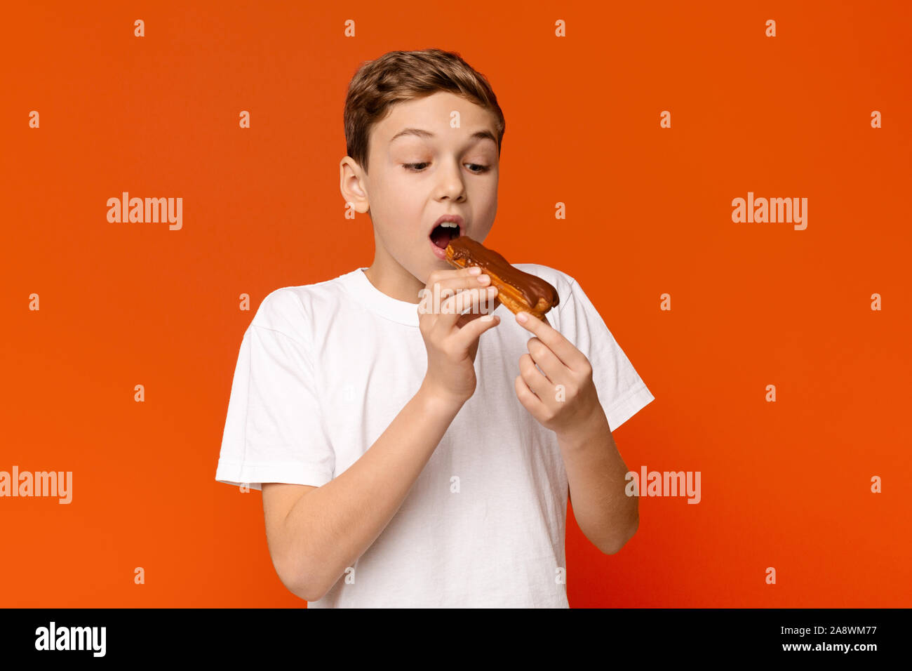 Teenage guy enjoying chocolate eclair, orange background Stock Photo