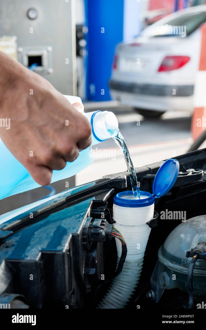 closeup of a young caucasian man pouring windshield washer fluid into the windshield washer fluid tank of a car Stock Photo