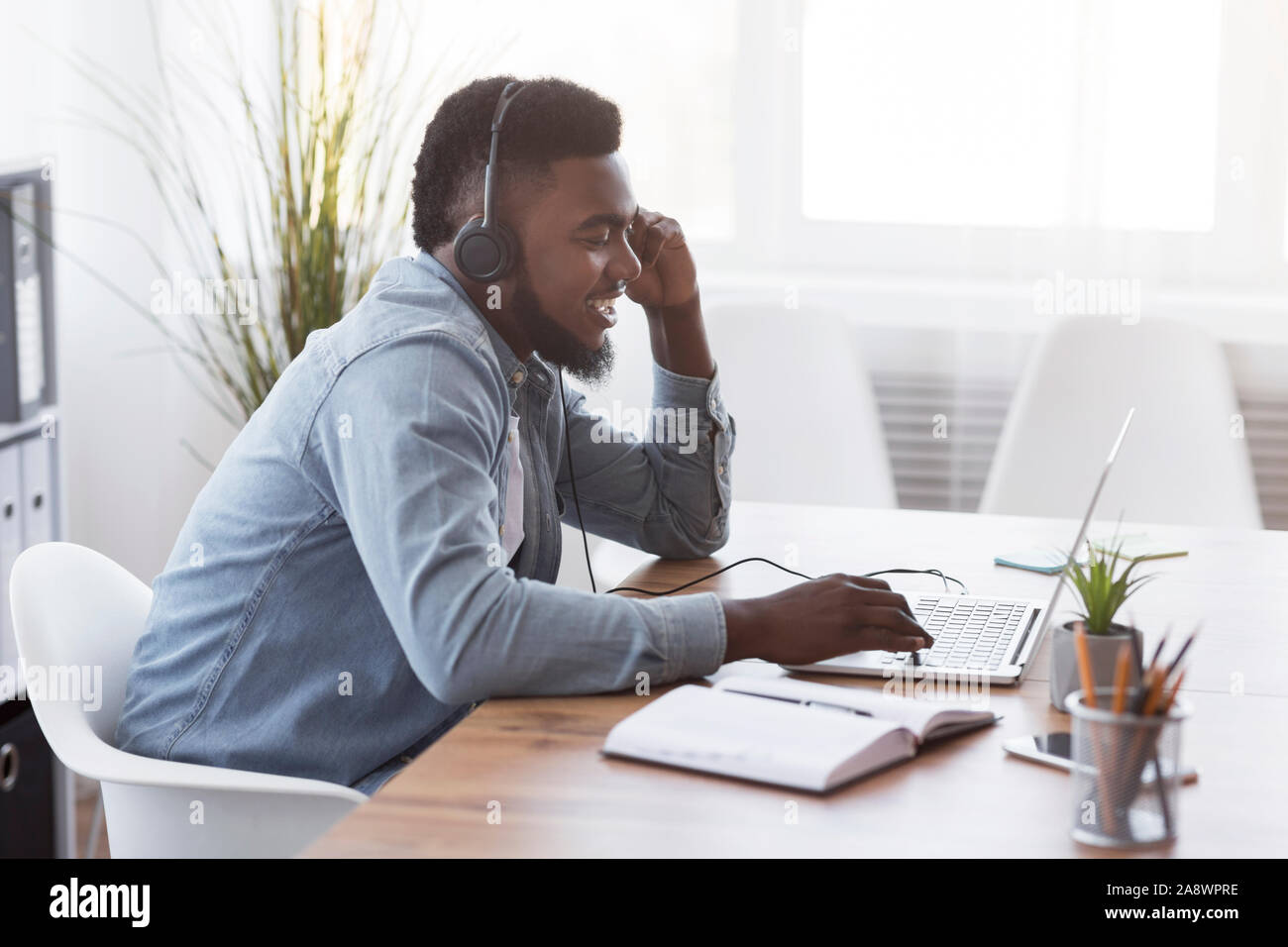 Cheerful manager wearing headset and using laptop, speaking with client Stock Photo