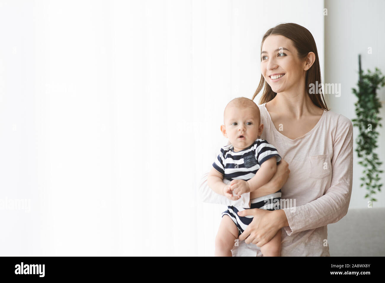 Happy mother holding newborn baby and looking out the window Stock Photo