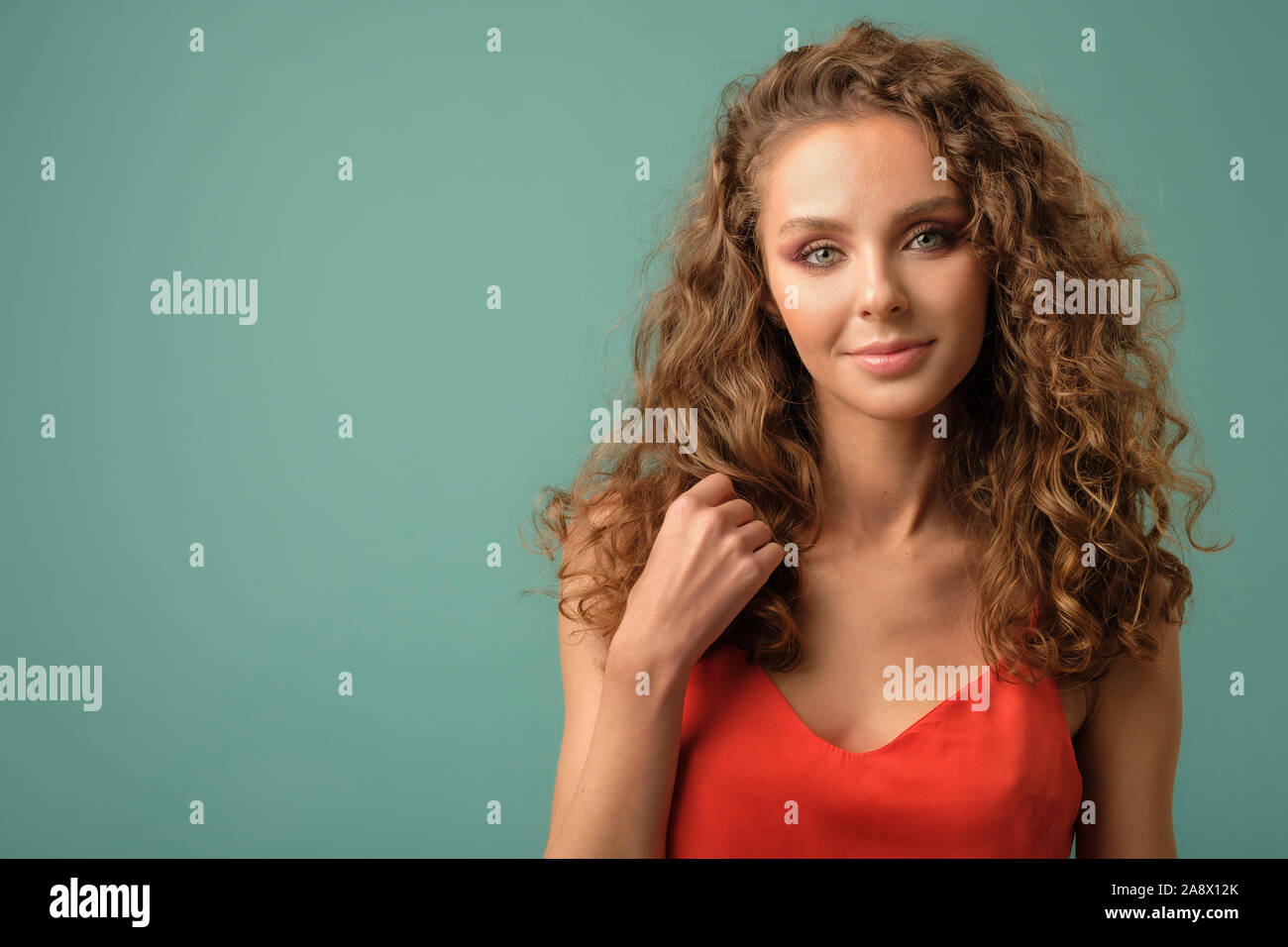 Closeup portrait of pretty caucasian girl with curly hair in red shirt posing in studio isolated on blue background Stock Photo
