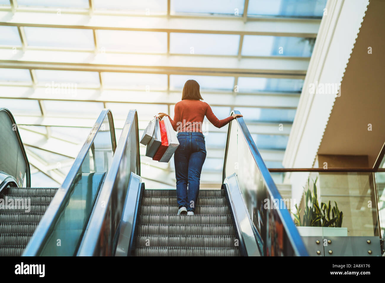 Young woman is walking on the escalator in a mall and shopping. Stock Photo