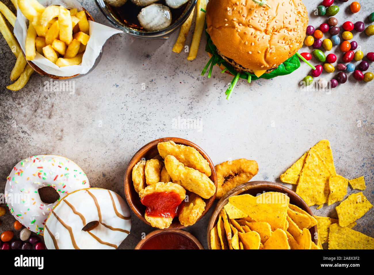 Assortment of fast food. Junk food background. Cheeseburgers, french fries, nachos, donuts, soda and nuggets on a gray background. Stock Photo