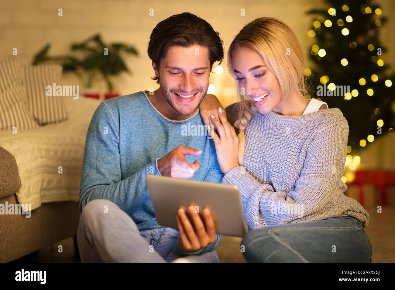 Loving couple using digital tablet next to Christmas tree Stock Photo